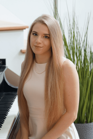 W&J alumna Caroline Fedor '20 sit on a piano bench and smiles.